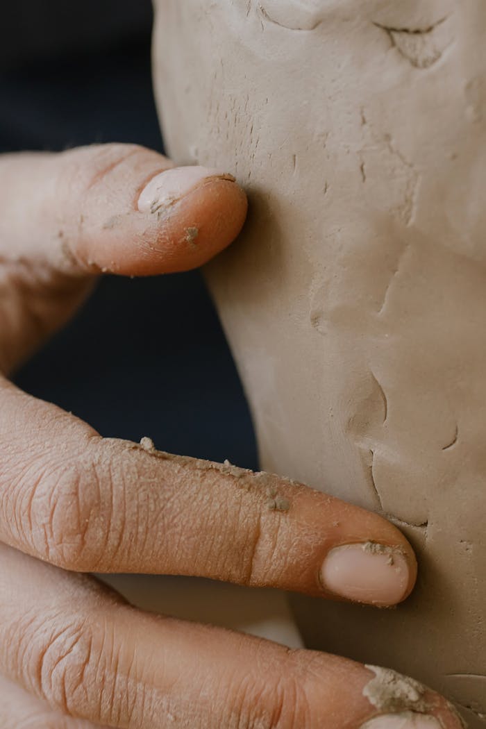 Detailed view of hands molding wet clay into pottery, showcasing craftsmanship.